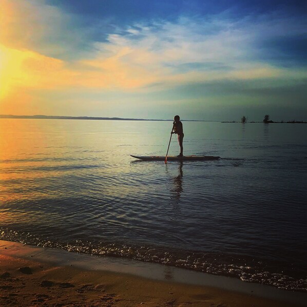 Eine Person steht bei Sonnenuntergang auf einem Paddleboard auf ruhigem Wasser.