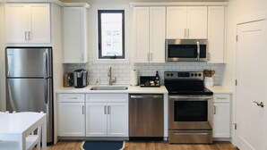 A modern kitchen with white cabinets, stainless steel appliances, a dishwasher, and a window above the sink. - Luxury Downtown Traverse City Condo-Capri 2 (Traverse City)