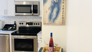 A kitchen with white cabinets, a stainless steel microwave, a double oven, and a wooden tray with a bottle and glasses. - Luxury Downtown Traverse City Condo-Capri 2 (Traverse City)