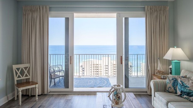 A room with a balcony overlooking the sea, a chair, a sofa, and a lamp. - TOO BEAUTIFUL GULF and SUNSET VIEWS! (Panama City Beach)
