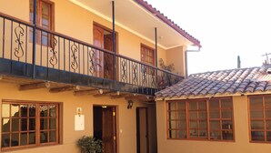 A two-story building with a balcony, a tiled roof, and a potted plant in front. - Alpaca Lodge (Chinchero)