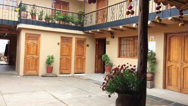 A courtyard with a wooden door, potted plants, and a balcony with hanging decorations. - Alpaca Lodge (Chinchero)