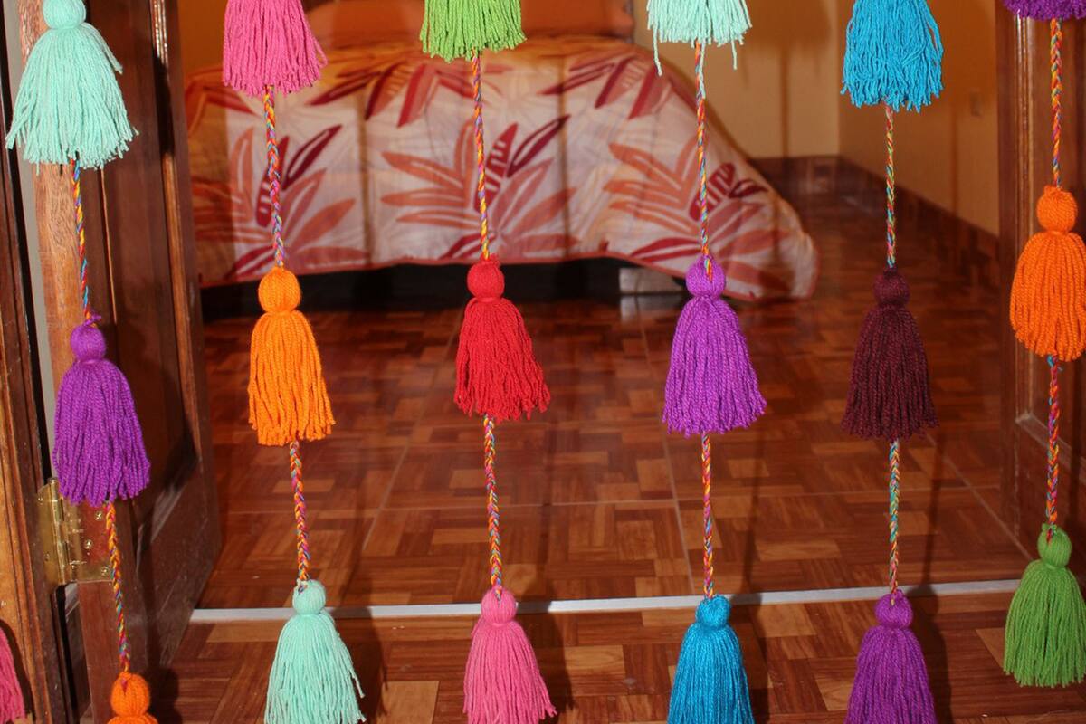 Una habitación con una cama, flecos coloridos colgando del techo y un tapete estampado en el suelo.
