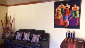 A living room with a black leather sofa, striped pillows, a colorful painting, and traditional pottery on a small table. - Alpaca Lodge (Chinchero)