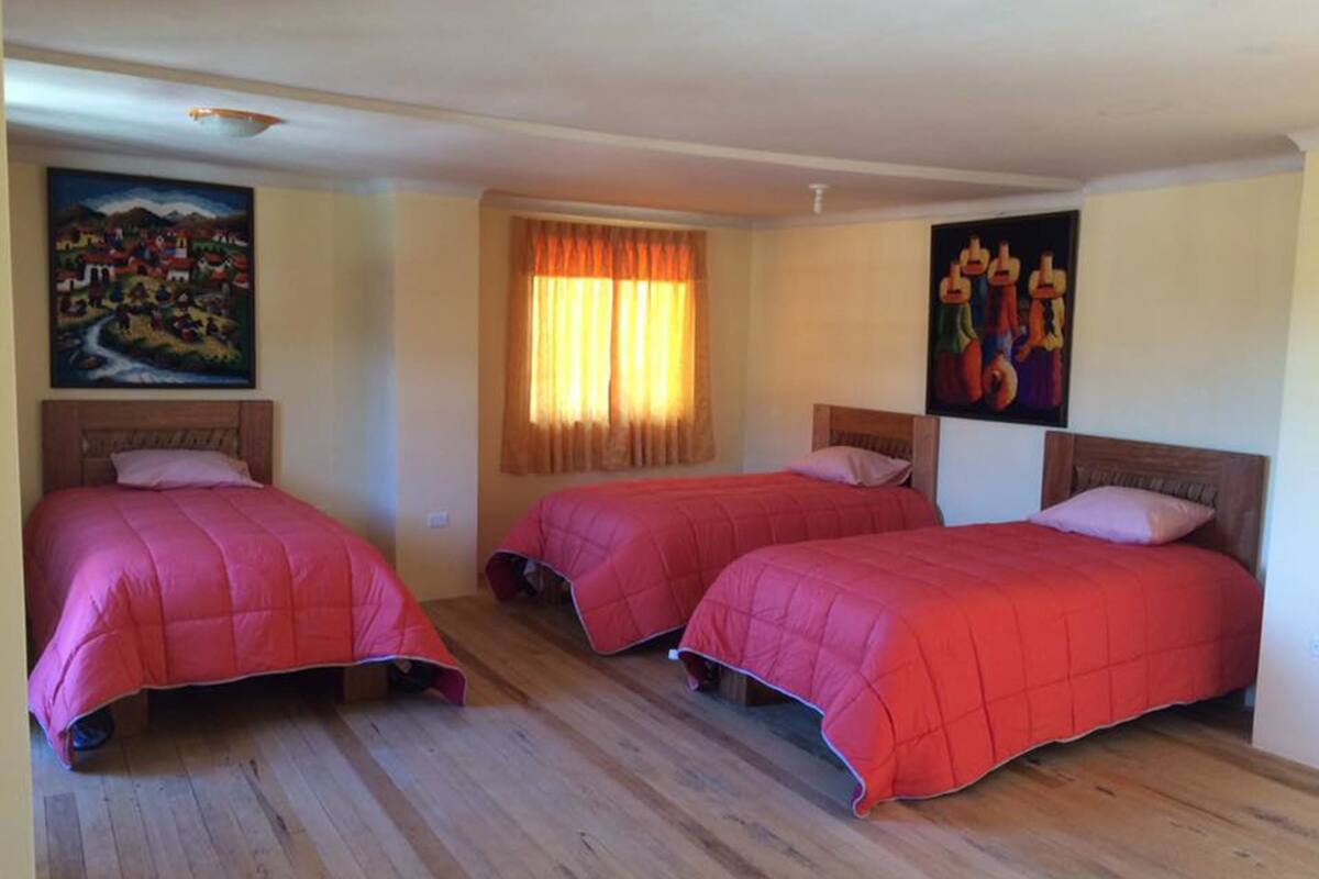 Una habitación con tres camas, suelo de madera y dos cuadros en las paredes.
