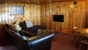 A wooden-paneled room with a black leather sofa, a small table, and a TV mounted on the wall. - Eagle Nest Fly Shack and Lodge (Eagle Nest)