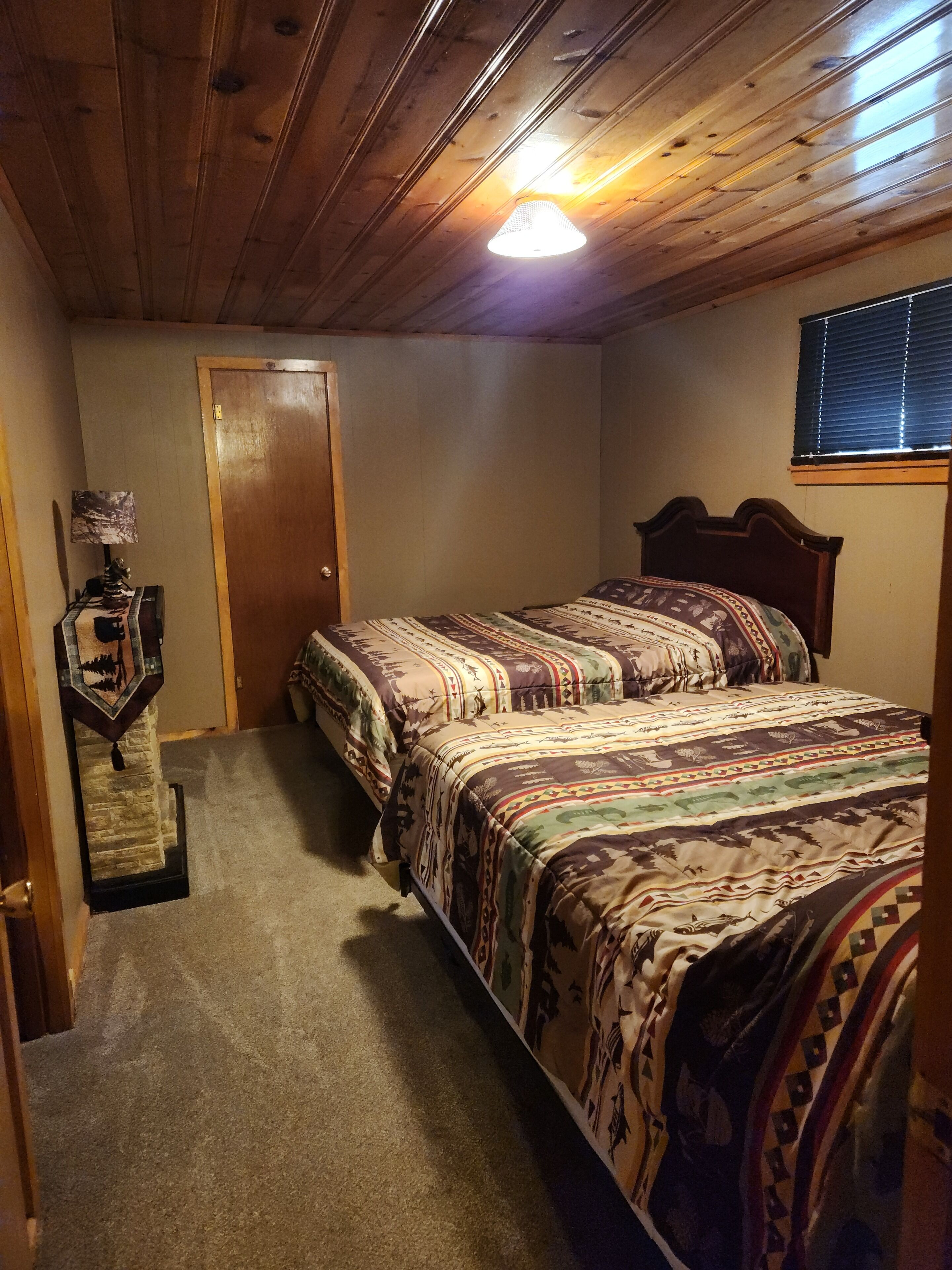 Un dormitorio con dos camas, techo de madera, una puerta y una ventana con persianas.