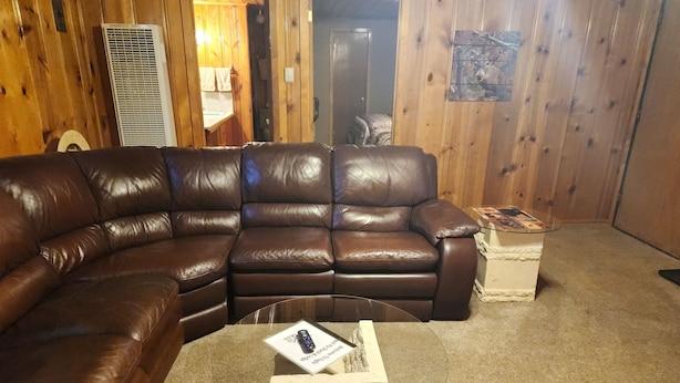 A brown leather sectional sofa, a glass coffee table with a remote control, and a small white side table with a magazine. - Eagle Nest Fly Shack and Lodge (Eagle Nest)
