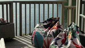 Una terraza de madera con vistas a un lago y montañas. Hay sillones orejeros de colores en la terraza.