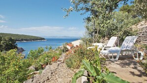A coastal view with a rocky foreground, a stone wall, and two white lounge chairs facing the sea.