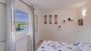 A bedroom with a bed, a window with curtains, a view of a body of water, and wall-mounted decor.