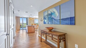 A spacious kitchen with a wooden island, a dining area with a table and chairs, and a view through the glass door to the outdoors. - Maui Resort Rentals: Honua Kai Hokulani 736 – 7th Floor Ocean & Mountain Views w/ King Size Balcony! (Lahaina)