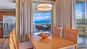 A dining area with a wooden table, striped cushions, and a decorative bowl. - Maui Resort Rentals: Honua Kai Hokulani 736 – 7th Floor Ocean & Mountain Views w/ King Size Balcony! (Lahaina)