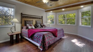 A bedroom with a wooden ceiling, a bed with plaid bedding, and multiple windows.