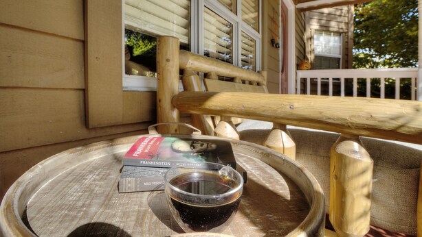 A wooden table with a glass of coffee, a book titled 'Frankenstein', and a metal cup.