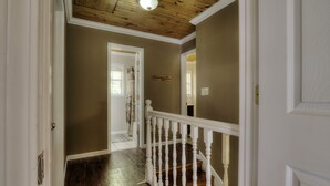 A hallway with wooden flooring, a white railing, and a ceiling with wooden beams.
