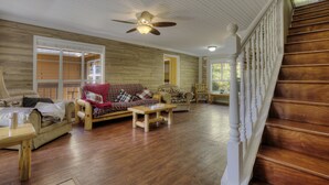 A spacious living room with wooden floors, a ceiling fan, and a staircase with white balusters.