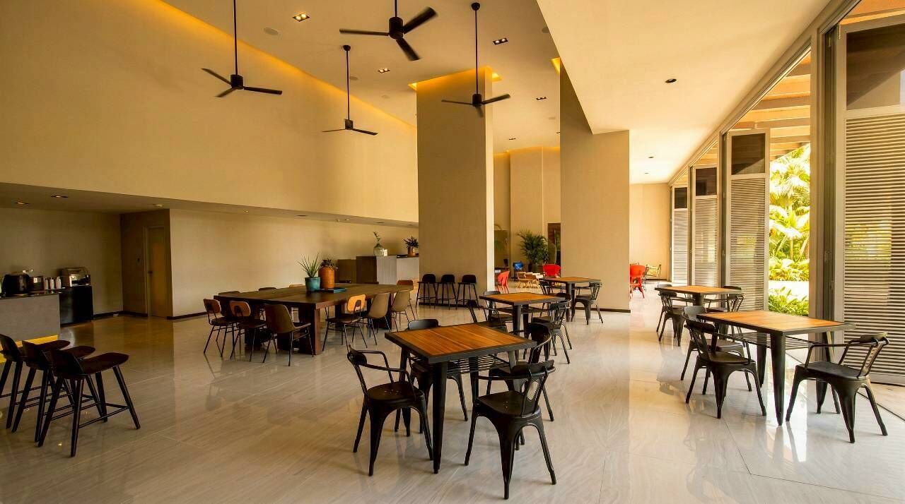 A spacious dining area with multiple tables and chairs, ceiling fans, and large windows allowing natural light.