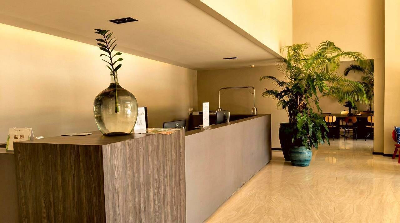 A reception desk with a vase, a large potted plant, and a dining area in the background.
