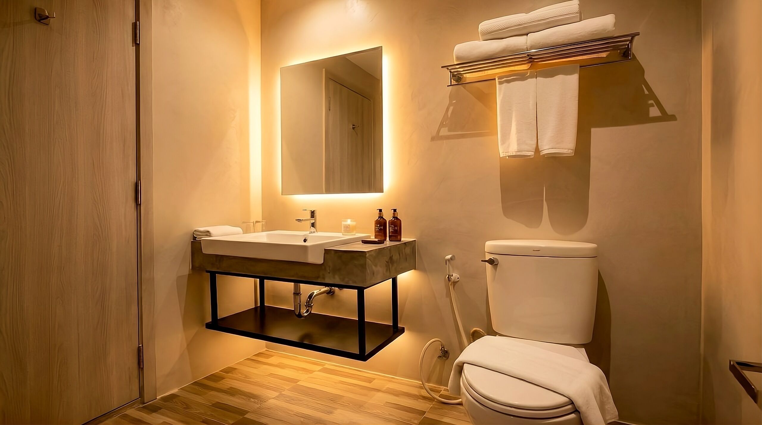Une salle de bain moderne avec un plancher en bois, un grand miroir, un lavabo avec des articles de toilette et des toilettes.