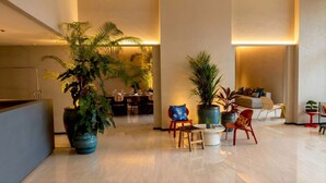 A spacious lobby with a modern design, featuring a dining area, seating arrangements, and large potted plants.