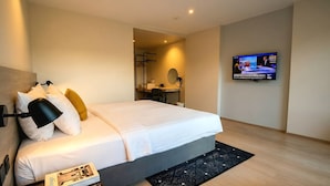 A modern hotel room with a neatly made bed, a desk with a chair, a television mounted on the wall, and a small mirror.
