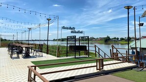 A lakeside deck with tables and chairs, a wooden ramp, and a sign with text.