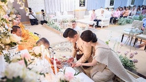 A room with a central table surrounded by guests, a white chair, and a sofa.