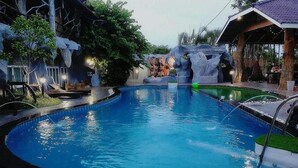 A swimming pool with a waterfall feature, surrounded by trees and a gazebo.