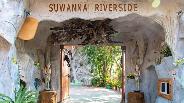 A cave-like entrance with a sign reading 'SUWANNA RIVERSIDE' and statues on wooden pedestals.