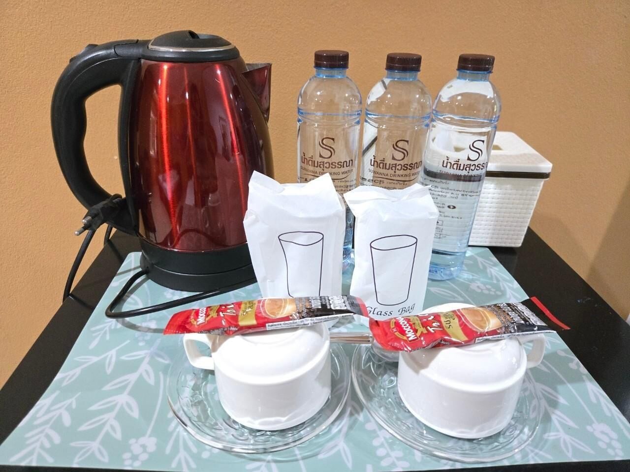 Una mesa con una tetera roja, botellas de agua, bolsas de vidrio y paquetes de bocadillos.