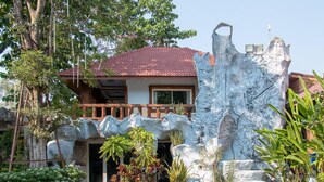 A house with a red-tiled roof, a balcony, and a rock-like structure in front.