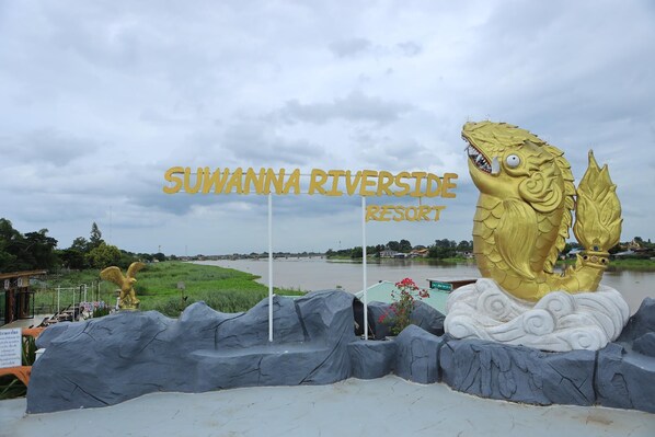 A sign for Suwanna Riveride Resort with a large golden fish statue.