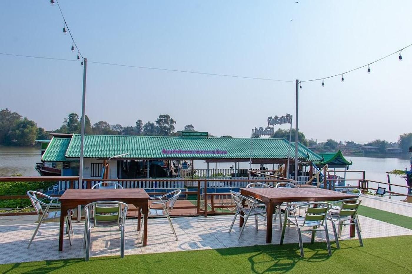 A riverside restaurant with outdoor seating, a green roof, and a view of the water.