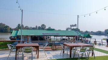 A riverside restaurant with outdoor seating, a green roof, and a view of the water.