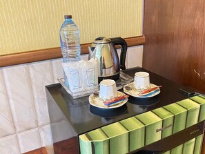 A hotel room's breakfast setup with a water bottle, glass cups, a kettle, and a tray of pastries.