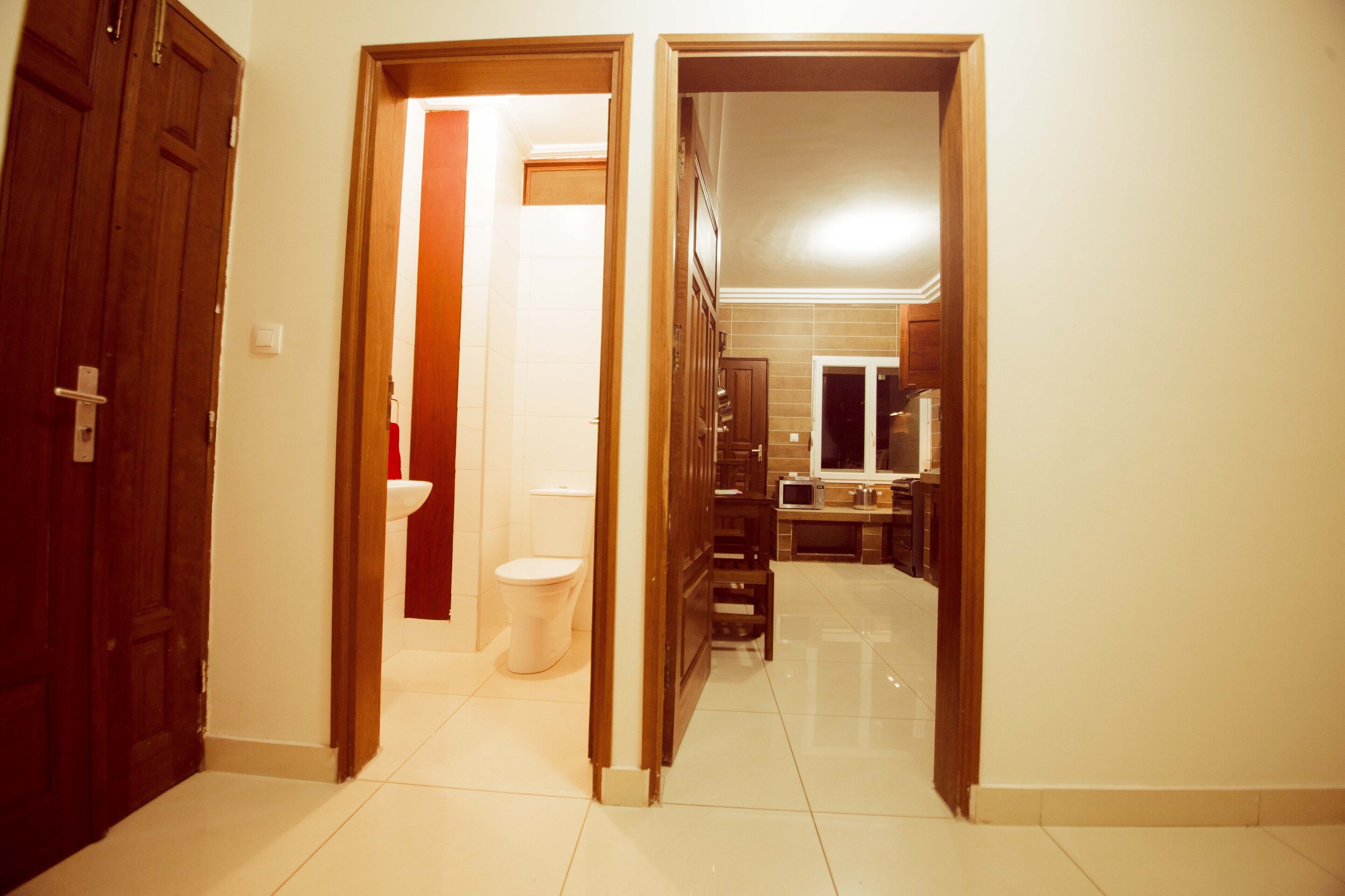 A hallway leading to a bathroom with a toilet and sink, and a kitchen area with cabinets and a microwave.