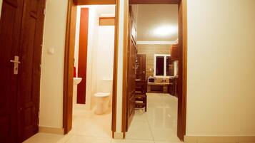 A hallway leading to a bathroom with a toilet and sink, and a kitchen area with cabinets and a microwave.