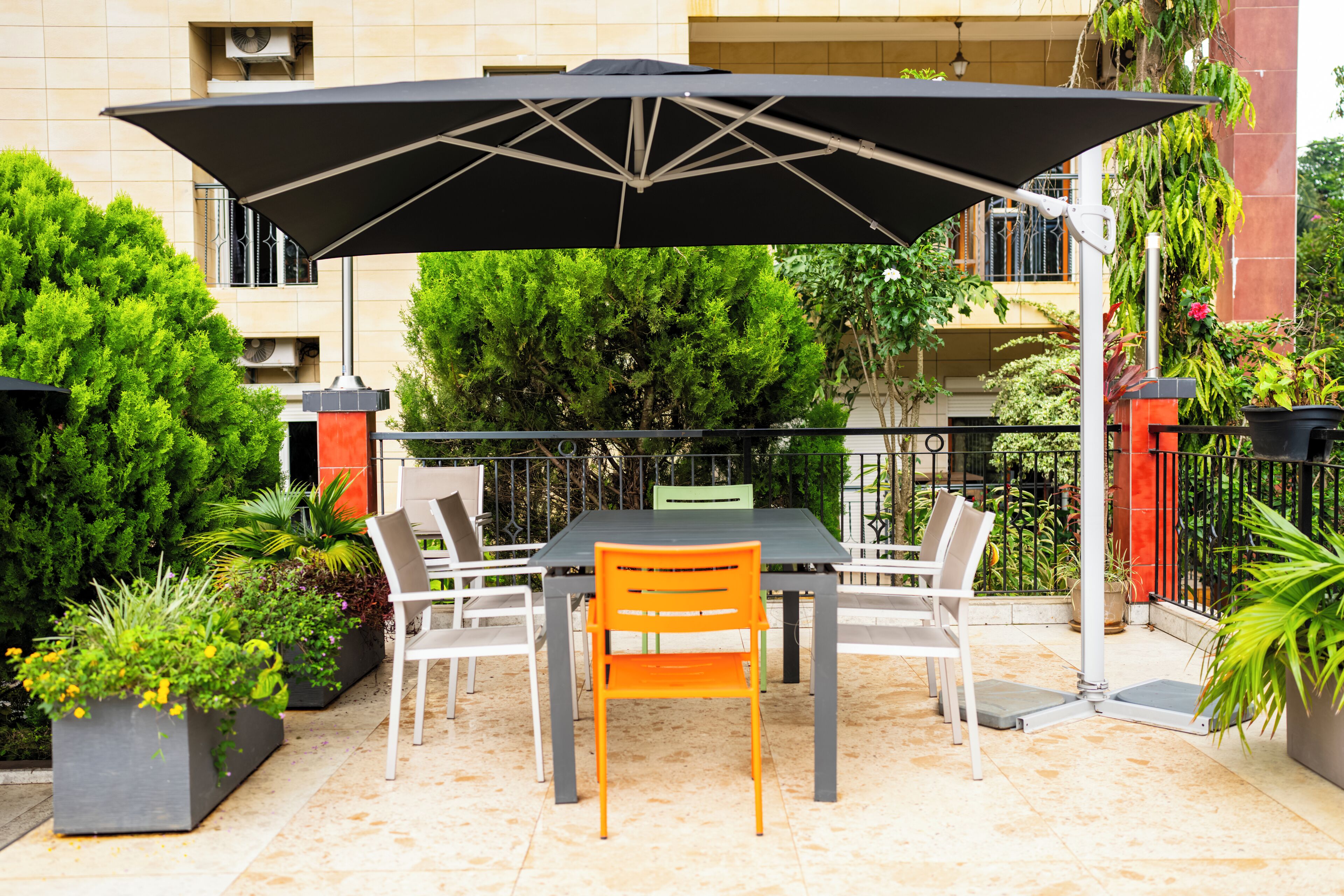 An outdoor patio with a table and chairs, surrounded by potted plants and a large umbrella.