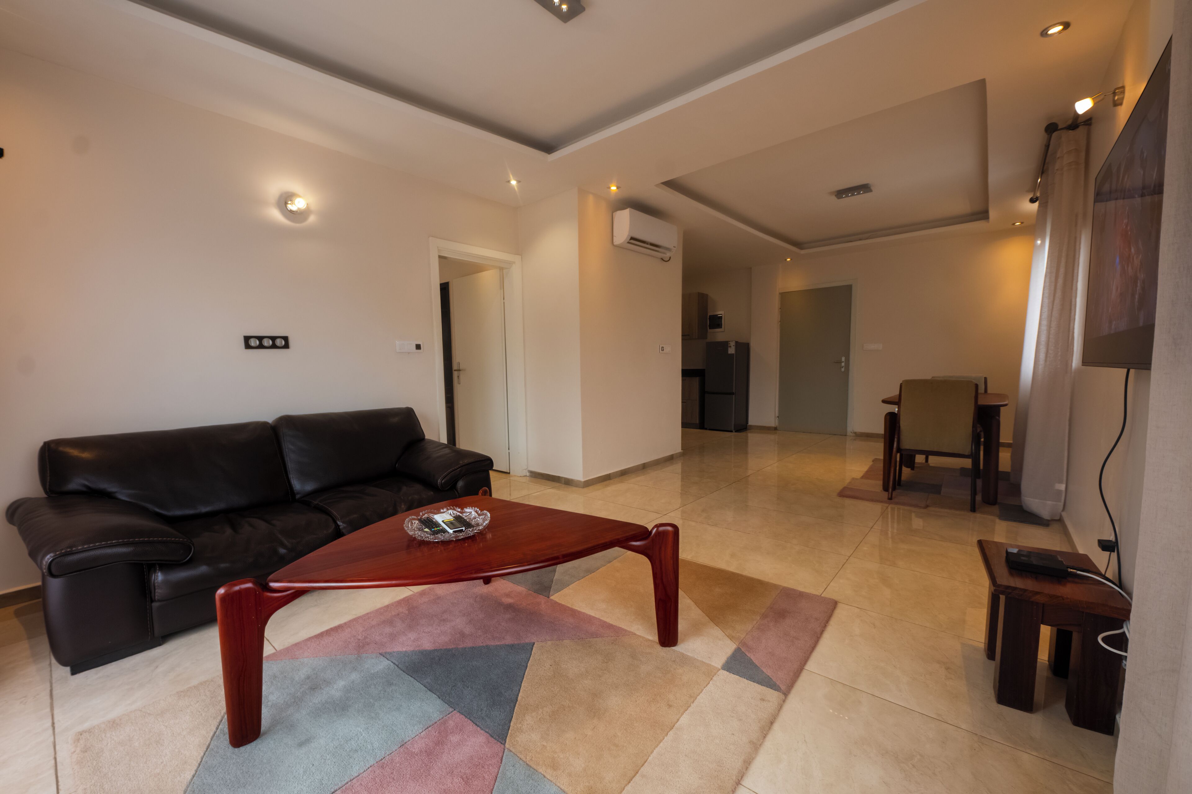 A living room with a brown leather sofa, a wooden coffee table, and a colorful rug.