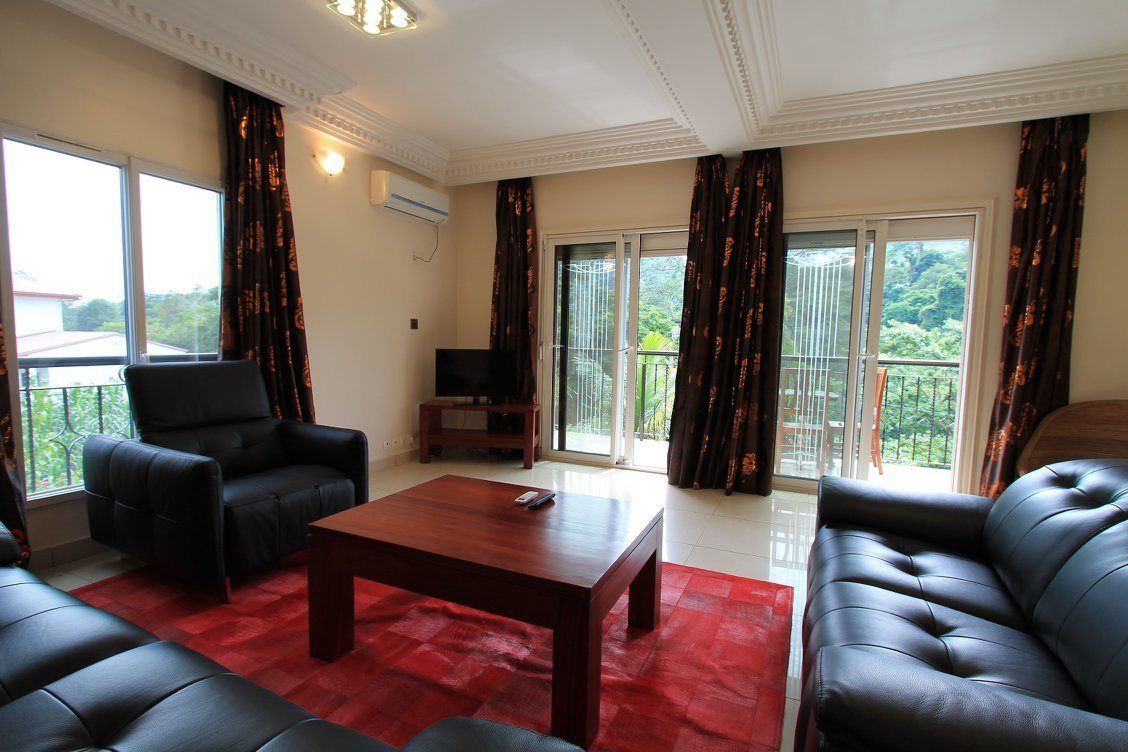 A living room with a red carpet, black leather sofas, a wooden coffee table, and a TV stand.