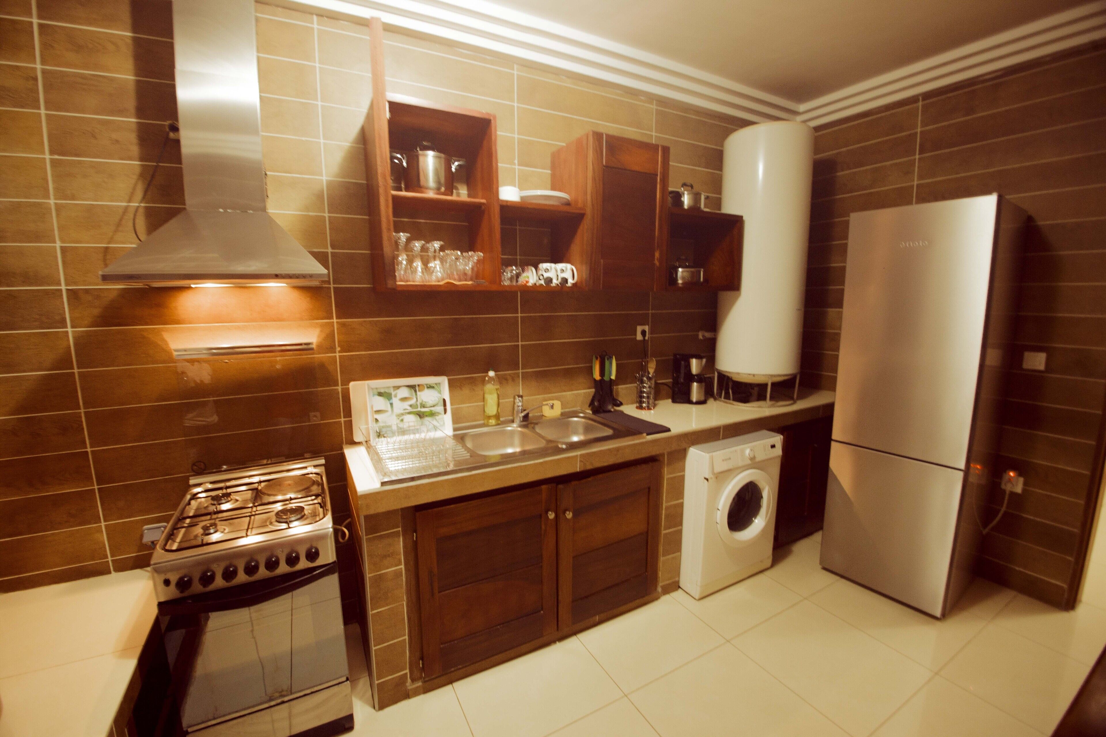 A kitchen with a stove, sink, washing machine, and refrigerator.
