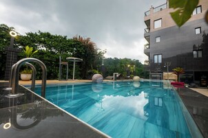 Piscina com design moderno, rodeada por área ajardinada com plantas em vasos e um edifício ao fundo.