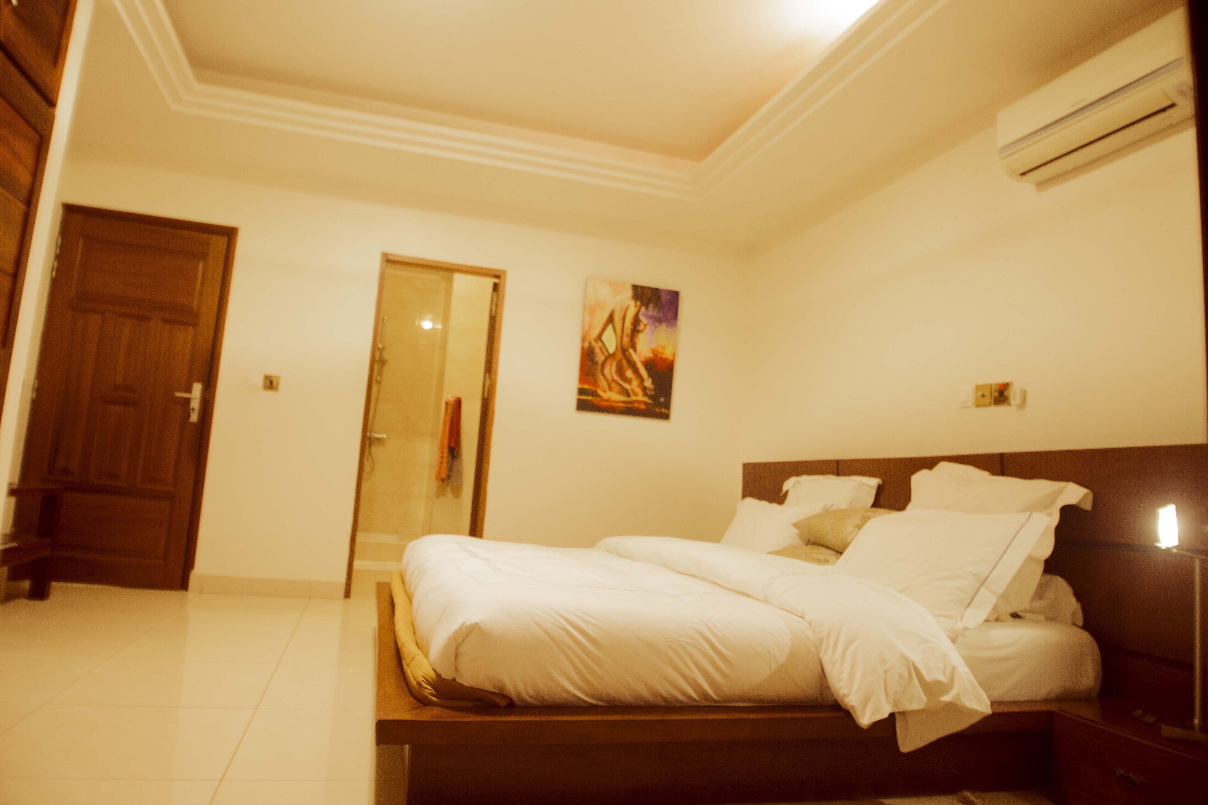 A bedroom with a bed, a wooden headboard, a nightstand, and an air conditioning unit.