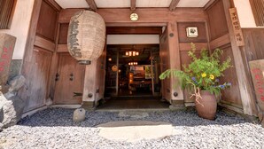 Une entrée traditionnelle en bois, avec une lanterne suspendue au-dessus de la porte, une plaque de pierre sur le côté gauche et un pot de fleurs sur le côté droit.