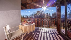 Une terrasse couverte avec une table dressée pour le repas, une chaise et une vue sur les arbres et le ciel.