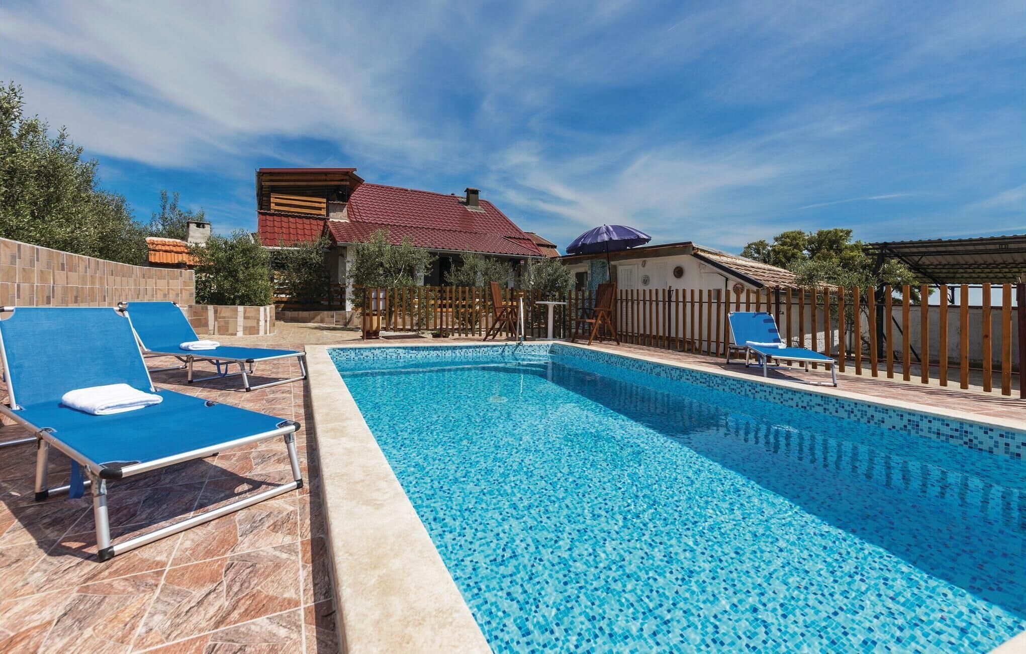 Una piscina con baldosas azules, rodeada de sillas de descanso y una valla de madera.