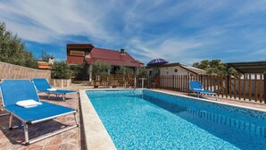 A swimming pool with blue tiles, surrounded by lounge chairs and a wooden fence.