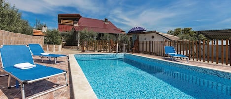 Una piscina con baldosas azules, rodeada de sillas de descanso y una valla de madera.
