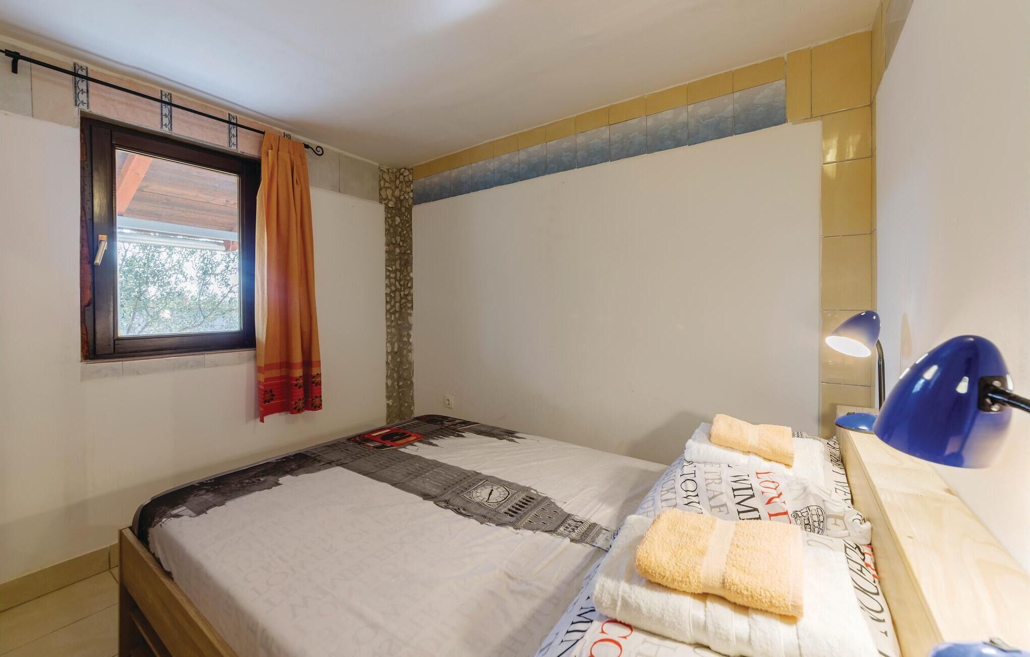 Une chambre à coucher avec un lit, une fenêtre avec des rideaux, une lampe et un mur orné d’un motif décoratif.